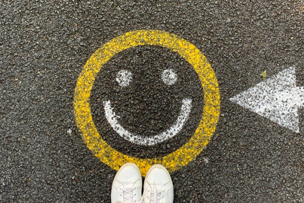 Painted smiley face and arrow on tar road with photographer's trainers showing